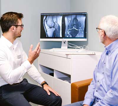 Radiologe Aachen erlärt Patient MRT-Bild an Bildschirm