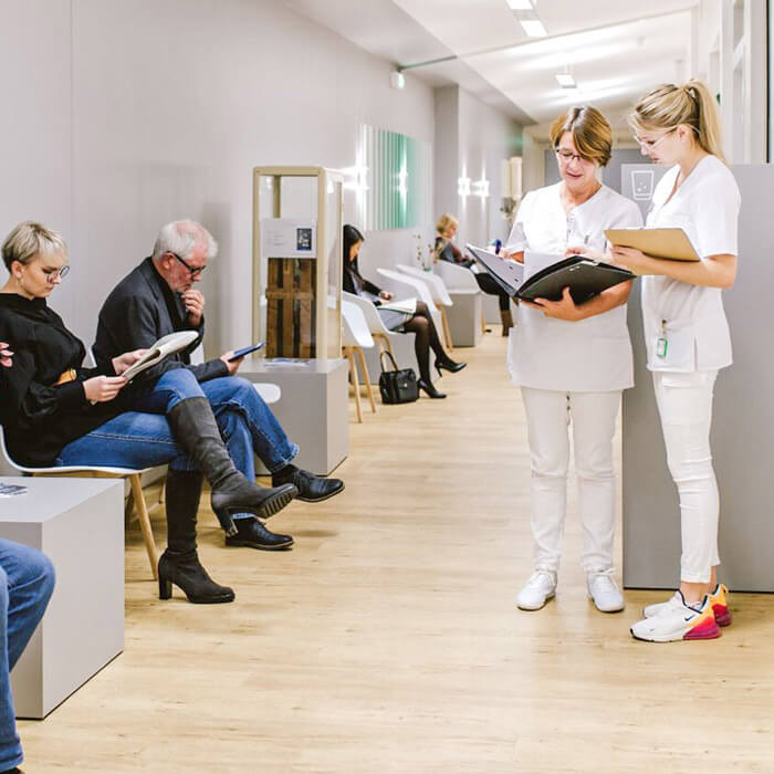 Patient:innen im Wartebereich der Radiologie Aachen, zwei Mitarbeiterinnen besprechen eine Akte.